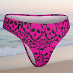 Pink swim bottoms with black skull and bone pattern on a faded beach background