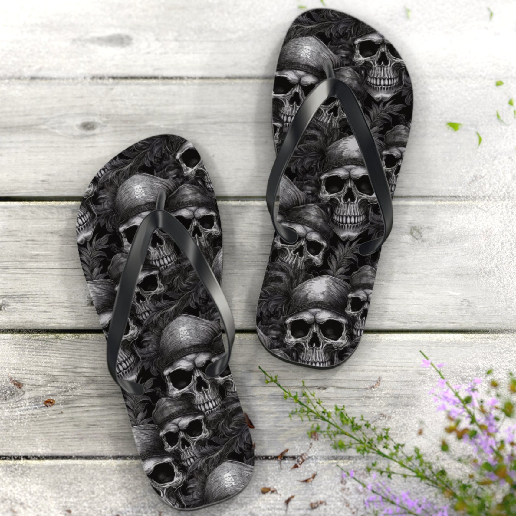 Flip-flops with pirate skull design on a wooden surface with flowers.