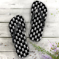 Flip-flops with skull and crossbones pattern on a wooden surface with flowers.