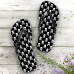 Flip-flops with skull and crossbones pattern on a wooden surface with flowers.