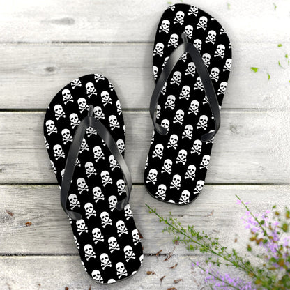 Flip-flops with skull and crossbones pattern on a wooden surface with flowers.