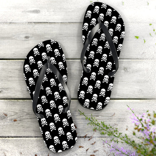 Flip-flops with skull and crossbones pattern on a wooden surface with flowers.