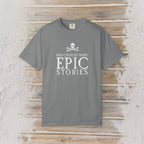 A gray short-sleeve Pirate T-Shirt with a white graphic print reading 'BAD CHOICES MAKE EPIC STORIES' and a skull and crossbones, laid flat on a rustic light wood background.