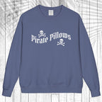 A slate blue crewneck sweatshirt featuring a white graphic print that reads 'Pirate Pillows' with skull and crossbones icons, displayed flat against a white wood plank background.