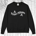 A black crewneck sweatshirt with a white graphic reading 'Pirate Pillows' and skull-and-crossbones icons, displayed flat against a white wood plank background.