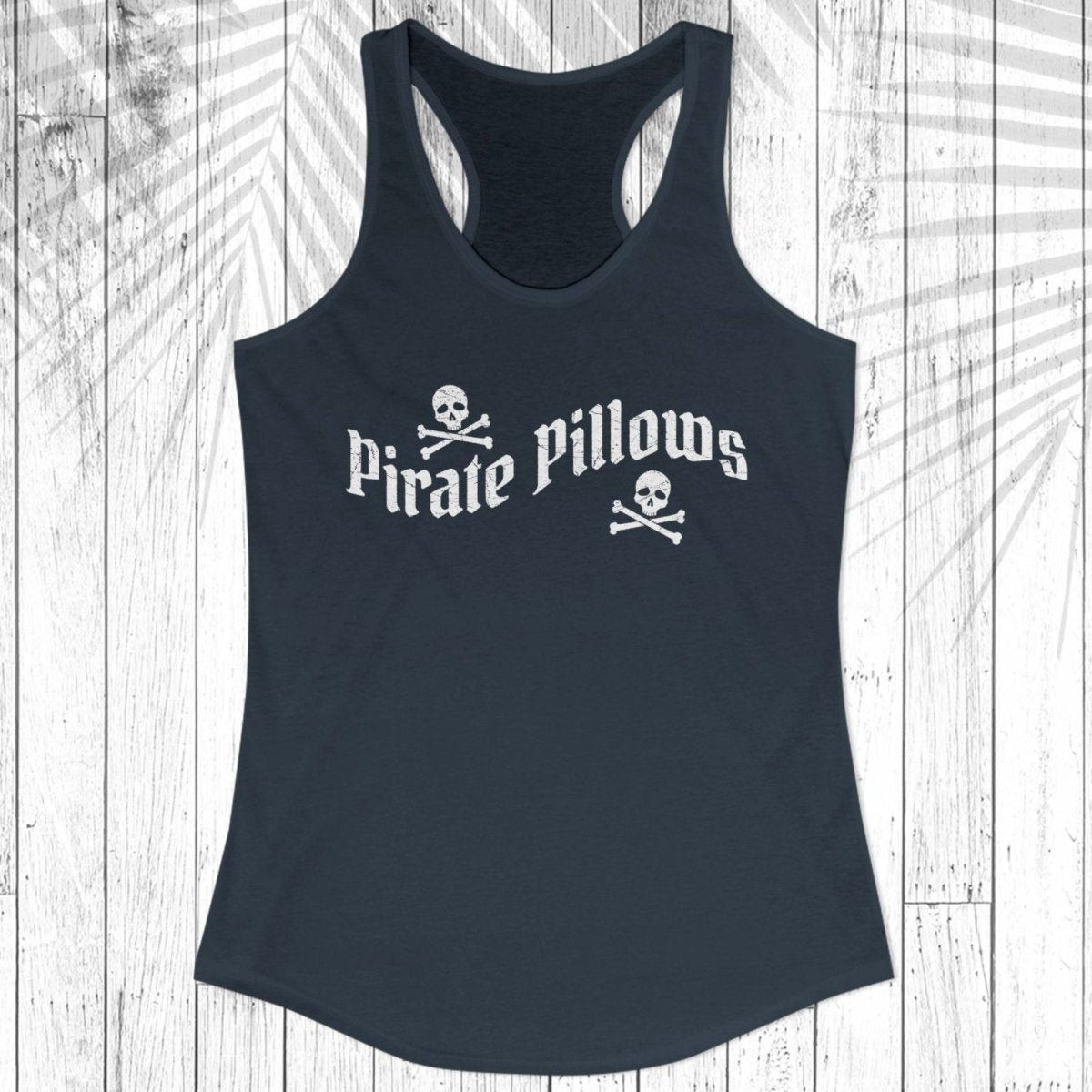 A black racerback tank top with 'Pirate Pillows' and skull-and-crossbones graphics on the front, displayed flat against a white wood plank background.