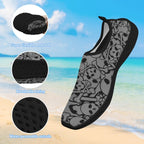 A gray and black slip-on water shoe with a skull-and-crossbones pattern, shown over a beach background with three circular detail callouts highlighting flexibility, breathable lining, and water-permeable outsole.