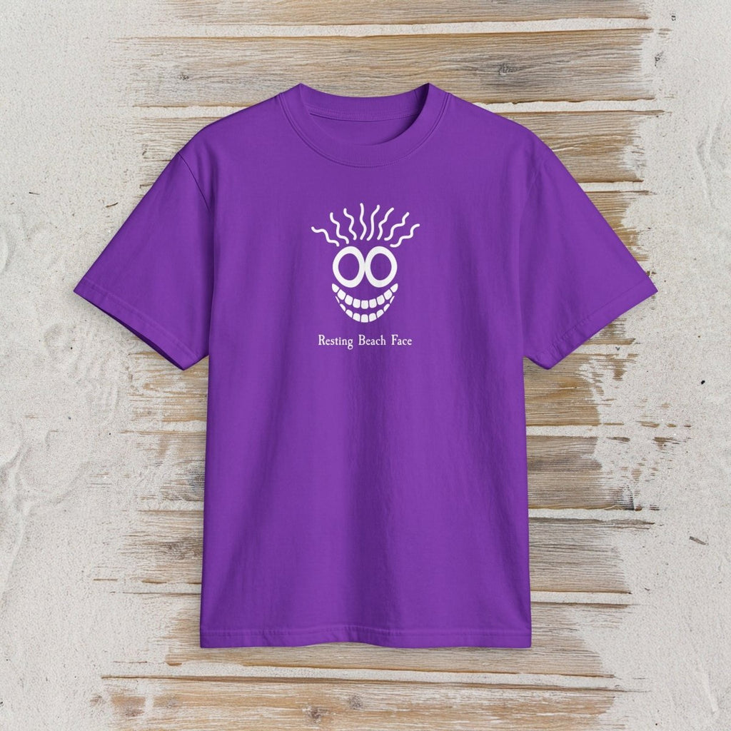 A purple short-sleeve crewneck t-shirt featuring a white graphic of a smiling face with sunglasses and the text 'Resting Beach Face' printed on the chest, displayed flat against a light-colored wooden plank background.