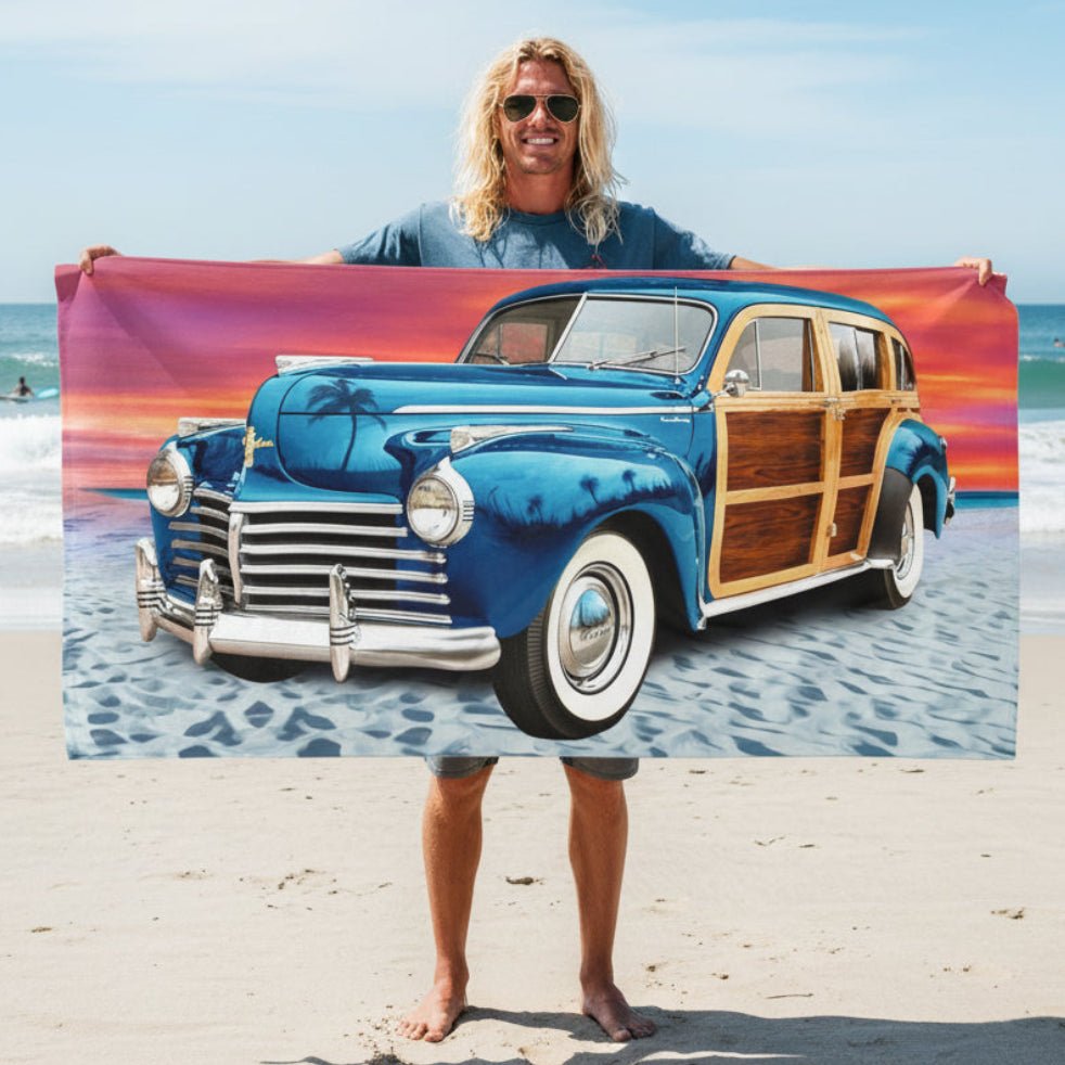 Surfer dude holding up a rectangular beach towel featuring a Vintage Woody Wagon on a sandy beach under a colorful sunset sky.