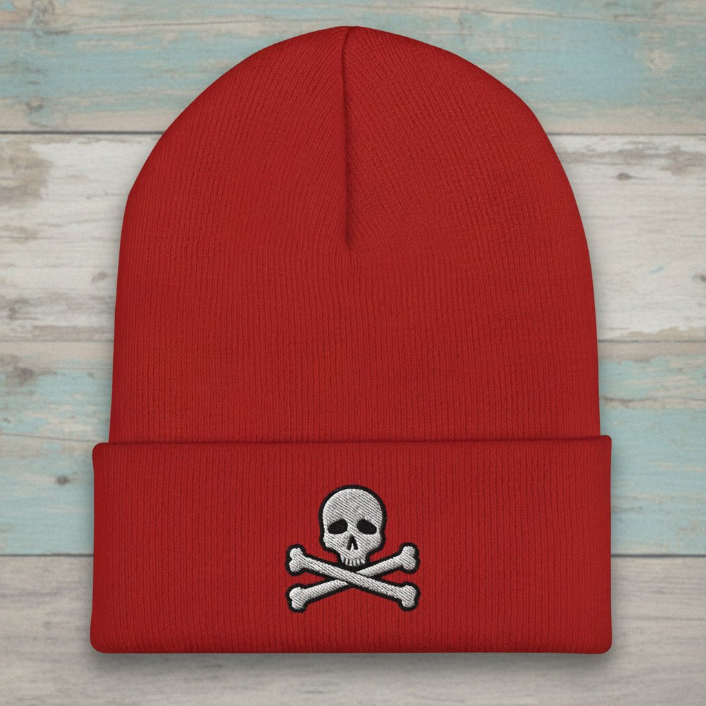A red knit beanie with a folded cuff featuring an embroidered skull and crossbones motif in gray and black, shown on a plain white background.