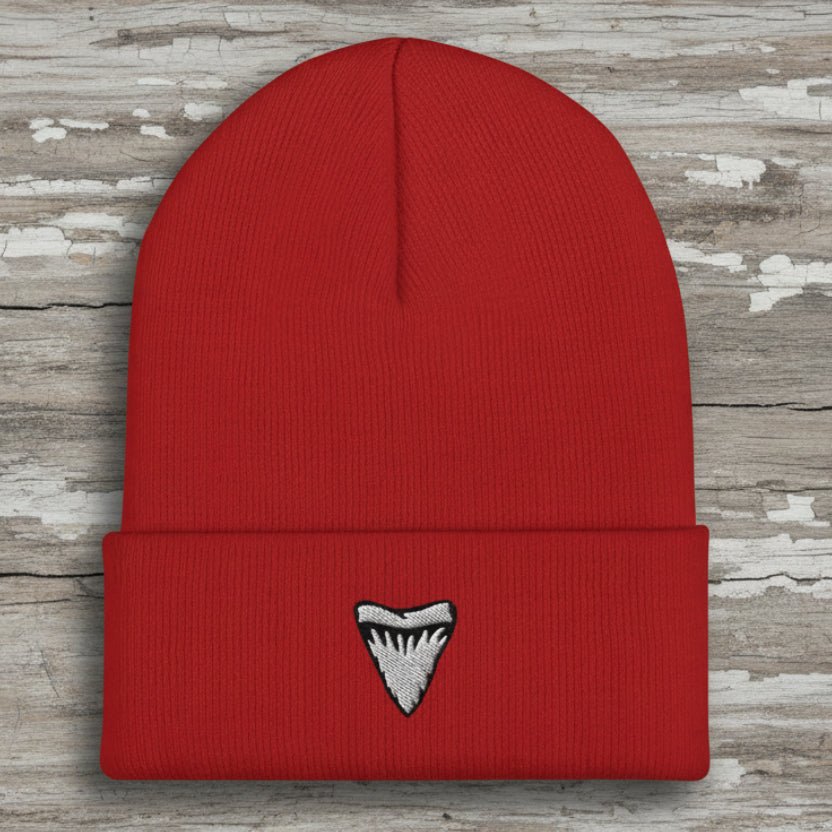 A red ribbed knit beanie with a folded cuff, featuring a small embroidered shark tooth logo in black and white on the front center.