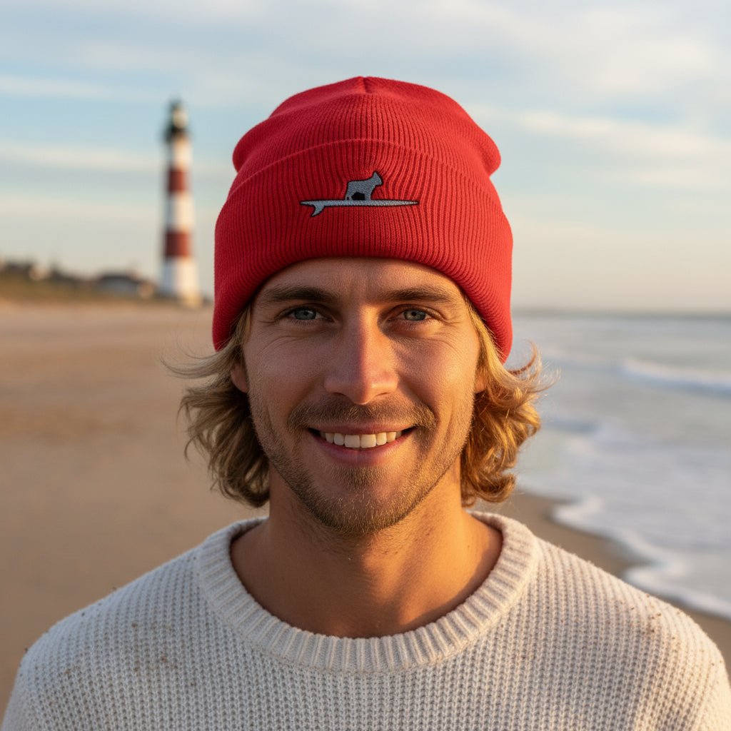 A red knit cuffed beanie hat featuring Surf Dog embroidered logo of a Frenchie standing on a surfboard on the front cuff, set against a plain white background.