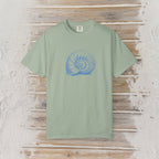 A sage green short-sleeve t-shirt with a blue spiral shell graphic on the chest, displayed flat on a rustic wooden plank background.