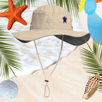 Beige bucket hat with a sea turtle embroidery on a beach-themed background with palm leaves, starfish, and shells.