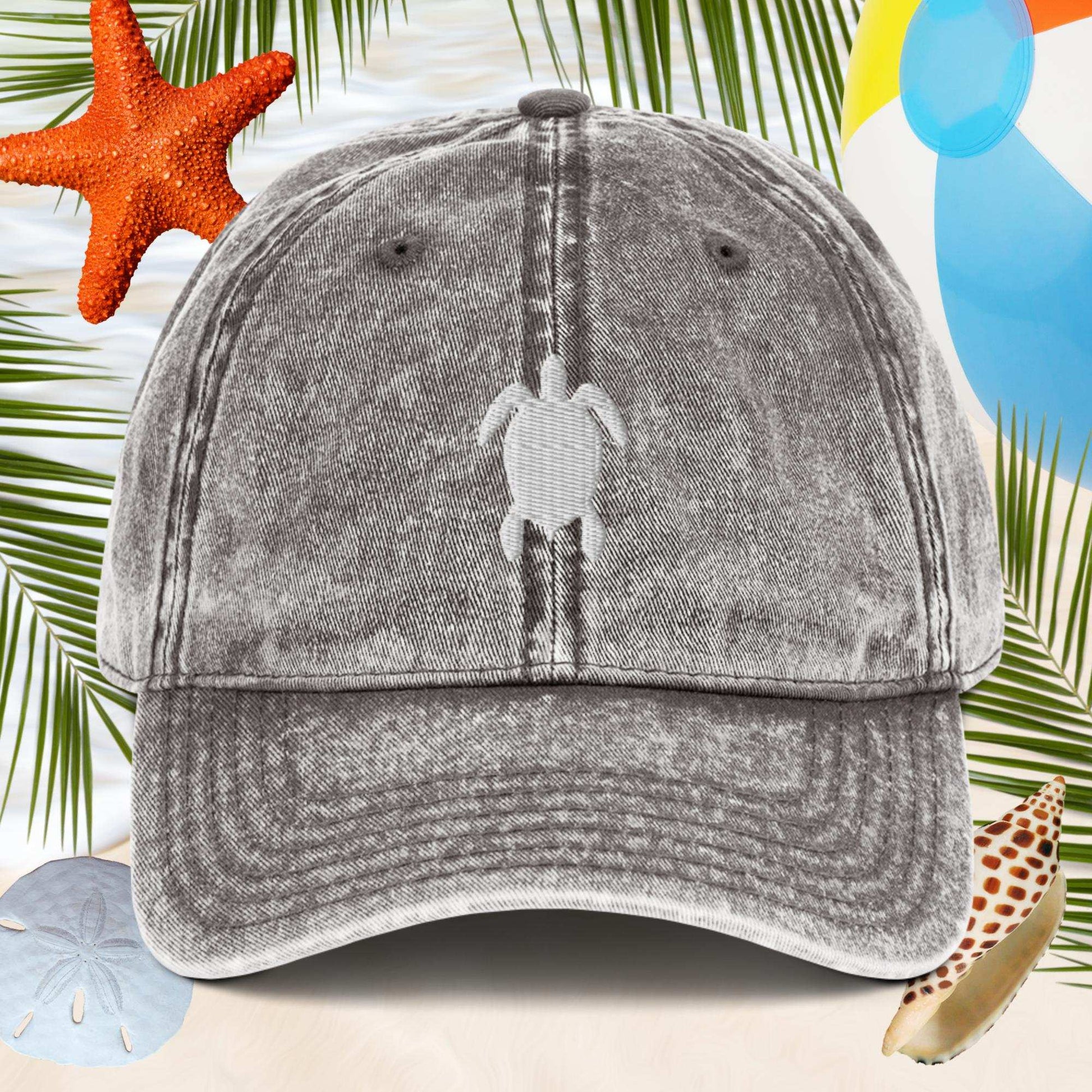 Gray cap with a turtle logo on a beach-themed background with starfish and palm leaves.