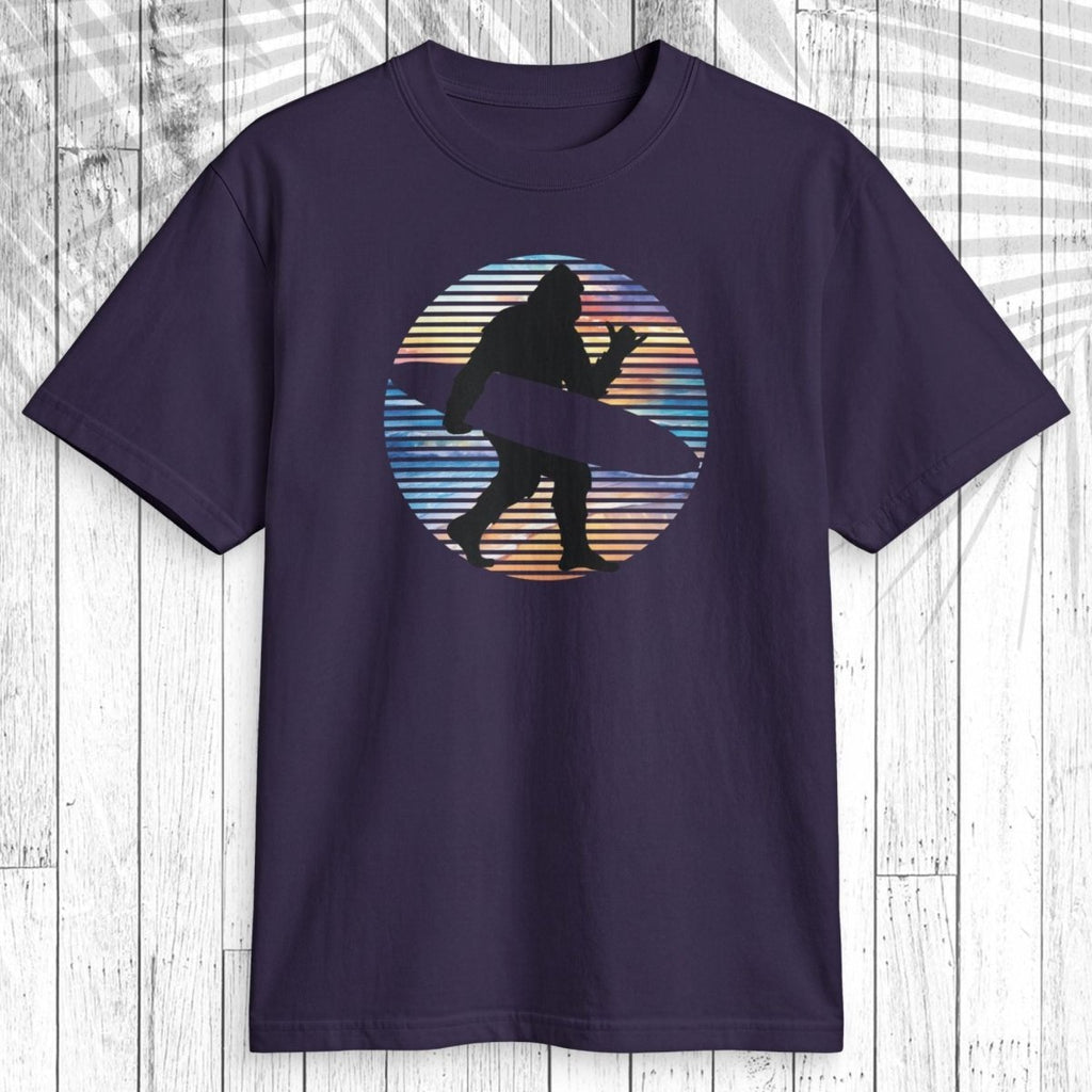 A dark navy short-sleeve t-shirt with a retro circular graphic of a surfer silhouette, displayed flat against a white wood plank background.