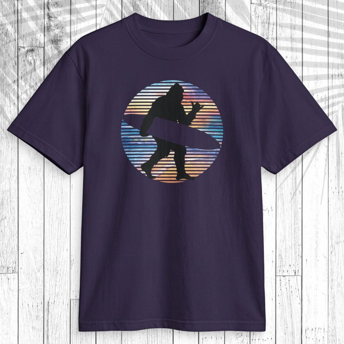 A dark navy short-sleeve t-shirt with a retro circular graphic of a surfer silhouette, displayed flat against a white wood plank background.