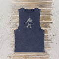 A sleeveless tank top in a washed navy blue color, featuring a light gray graphic of a Bigfoot silhouette carrying a surfboard, laid flat on a rustic wooden plank background.