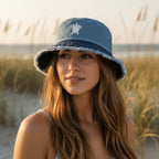 Beautiful woman wearing a blue bucket hat with white sea turtle embroidery standing in sand dunes with sea oats behind her