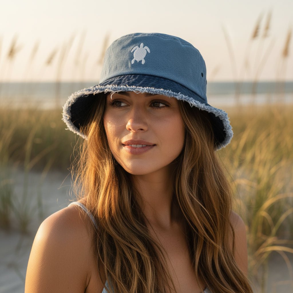 Beautiful woman wearing a blue bucket hat with white sea turtle embroidery standing in sand dunes with sea oats behind her