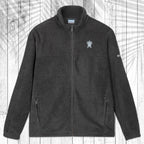 A dark gray fleece zip-up jacket with a stand collar, shown flat against a white wood plank background with a palm leaf pattern overlay. The jacket features a small white circular logo on the left chest and a small white logo on the right sleeve.