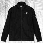 A dark gray fleece zip-up jacket with a stand collar, shown flat against a white wood plank background with a palm leaf pattern overlay. The jacket features a small white circular logo on the left chest and a small white logo on the right sleeve.