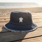 Navy blue bucket hat with white fringe on and a sea turtle embroidery sitting on a beachside boardwalk