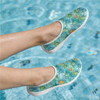 A pair of slip-on water shoes with a colorful sea turtle pattern, shown on feet in a swimming pool.