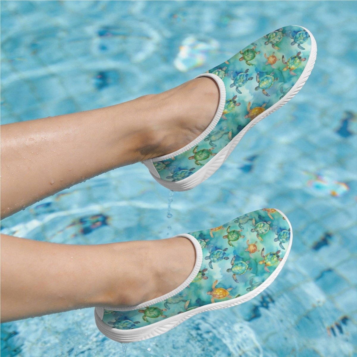 A pair of slip-on water shoes with a colorful sea turtle pattern, shown on feet in a swimming pool.