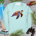 Light blue long-sleeve sun shirt with a colorful turtle design on a wooden background with beach-themed items.