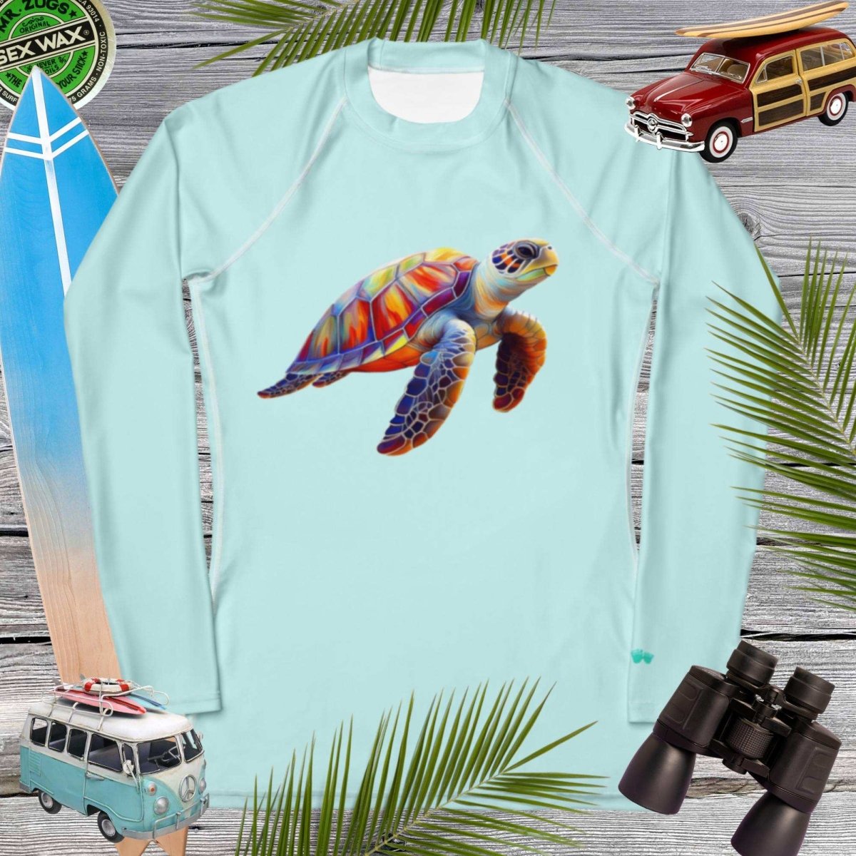 Light blue long-sleeve sun shirt with a colorful turtle design on a wooden background with beach-themed items.