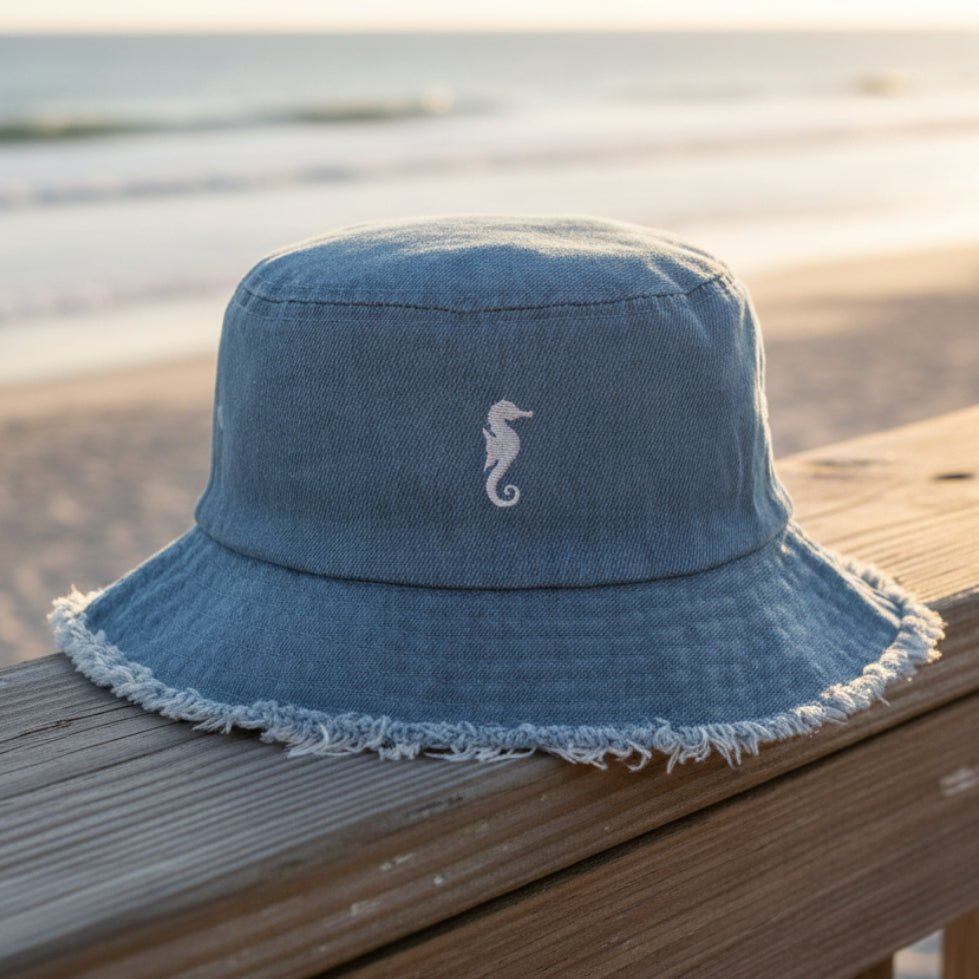 Blue denim bucket hat with a seahorse logo on a beachside boardwalk