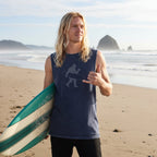A man wearing a sleeveless navy blue t-shirt with a gray graphic of surfing Sasquatch standing on the beach in seaside oregon