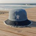 Blue bucket hat with white seaturtle embroidery on a beachside boardwalk