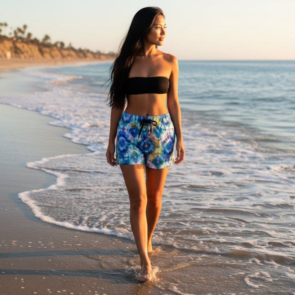 beautiful woman with long black hair walking along the waves in Malibu beach wearing colorful tie-dye shorts with a drawstring