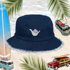 Shaka Blue Jean Bucket Hat with Hang Loose logo, perfect for surfers and stylish beachgoers, set against a tropical backdrop.