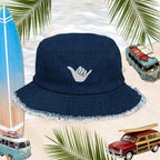 Shaka Blue Jean Bucket Hat with Hang Loose logo, perfect for surfers and stylish beachgoers, set against a tropical backdrop.