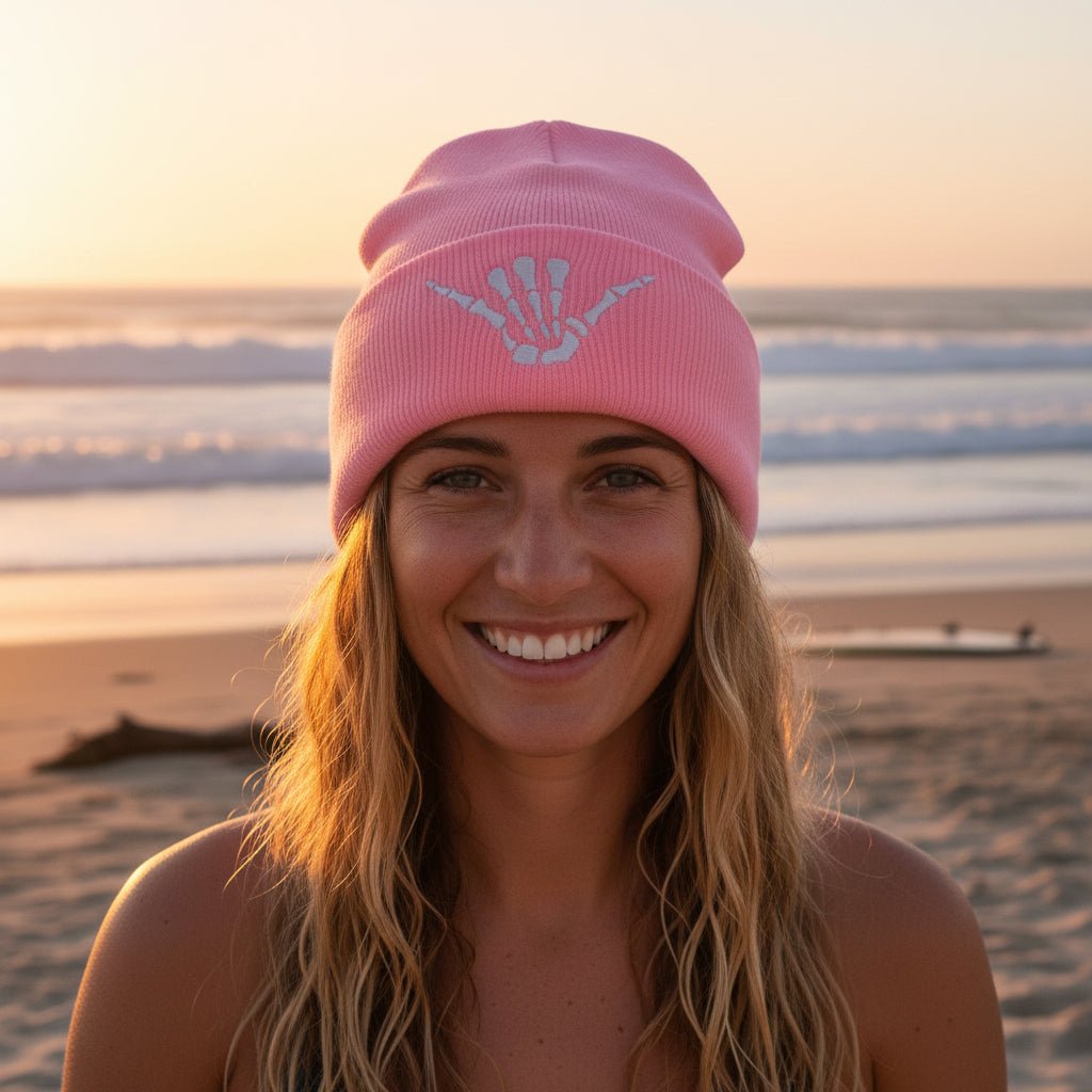 A light pink Hand of a Skeleton knit beanie hat with a folded cuff featuring an embroidered white skeleton hand design, shown on a clean white background.