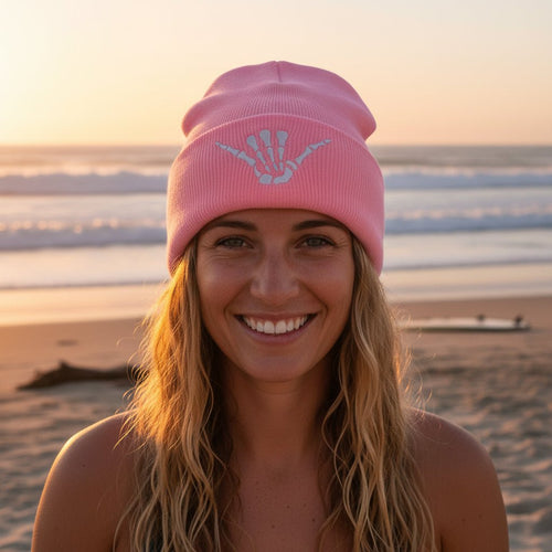 A light pink Hand of a Skeleton knit beanie hat with a folded cuff featuring an embroidered white skeleton hand design, shown on a clean white background.