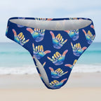 Blue shaka wear bikini bottoms with colorful hang loose shaka hand gesture pattern on a faded beach scene background