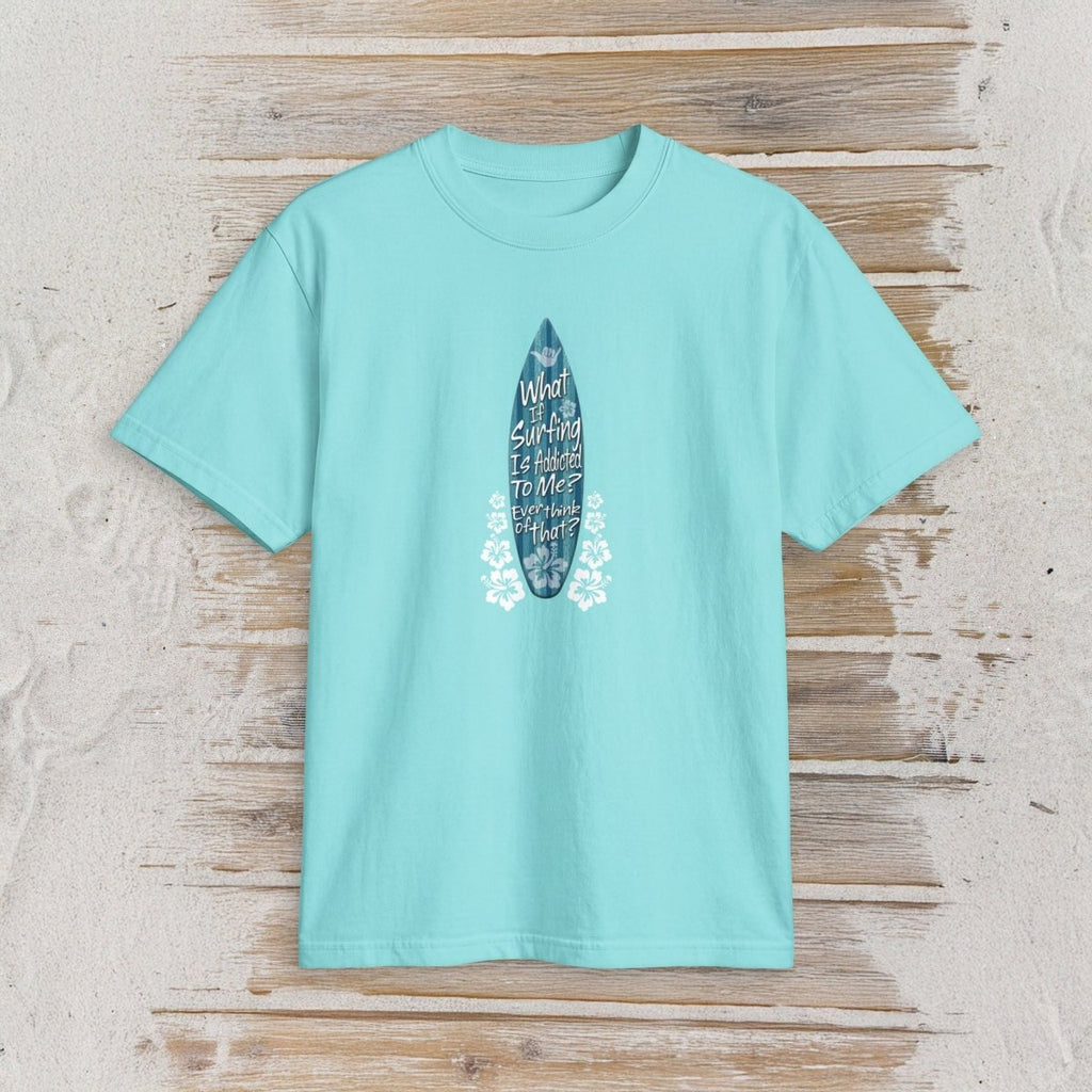 A light aqua blue short-sleeve t-shirt laid flat on a rustic light wood background. The center of the shirt features a graphic of a dark blue surfboard with white text reading 'Wait for Surfing to Be My Future' and white floral designs on either side.
