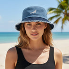 A woman on a sunny beach wearing a blue bucket hat with a white shark graphic and white frayed trim, paired with a black tank top.