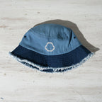 Blue bucket hat with frayed edge and embroidered shark jaw a nautical wood surface