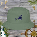 Green bucket hat with shark design on a wooden background with ship wheel and lighthouse.