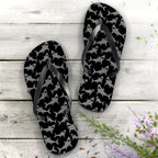 Black and gray patterned flip-flops on a wooden surface with flowers.