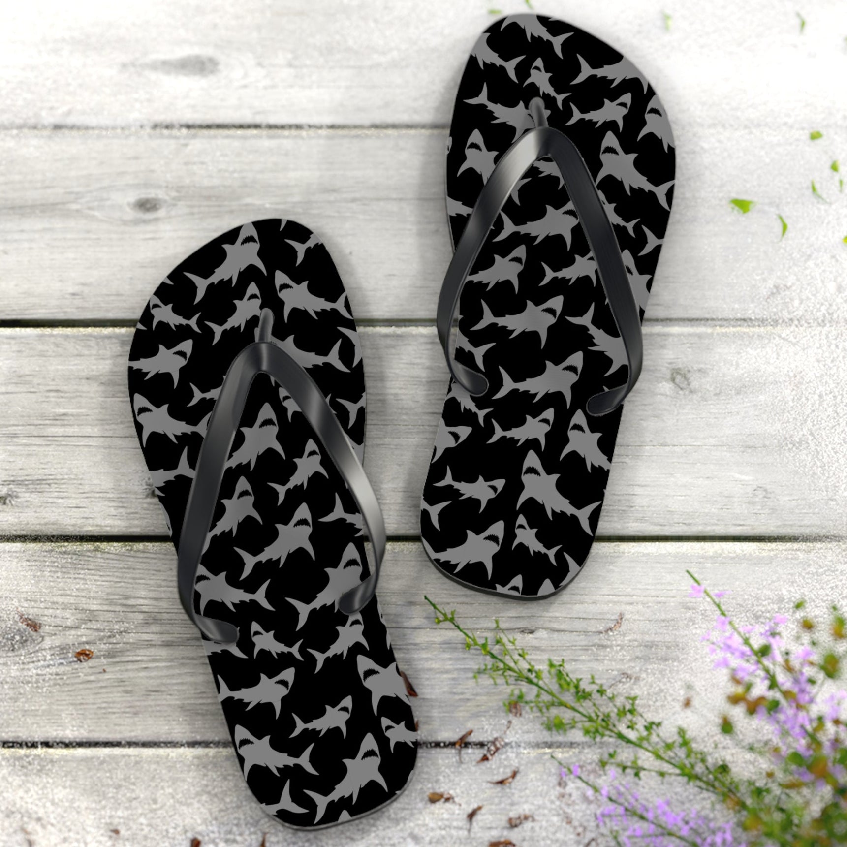 Black and gray patterned flip-flops on a wooden surface with flowers.