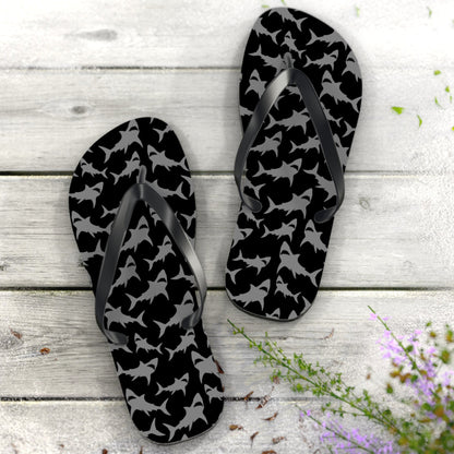 Black and gray patterned flip-flops on a wooden surface with flowers.