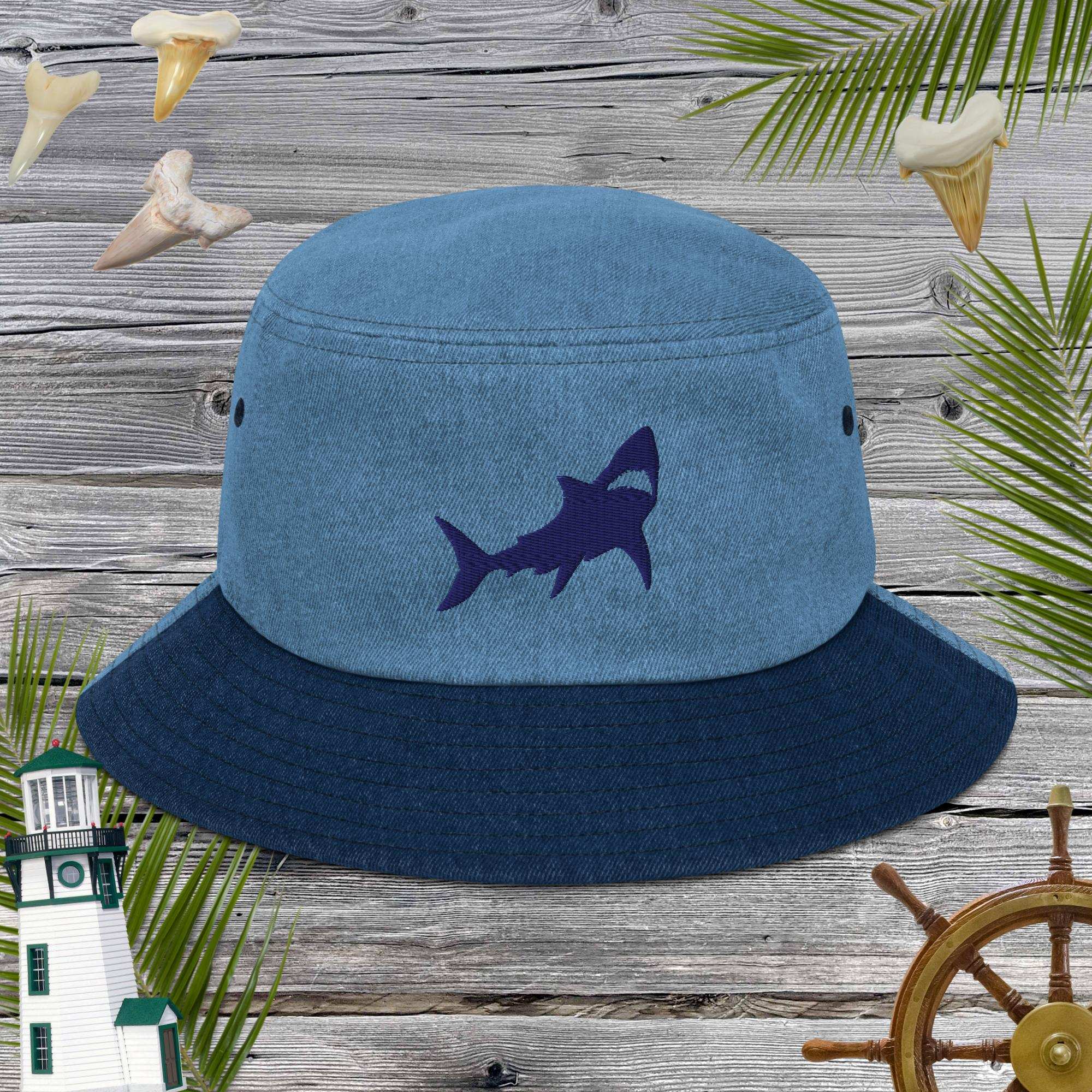Blue bucket hat with shark embroidery on a wooden background with nautical elements.