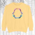 A pale yellow crewneck sweatshirt featuring a colorful graphic of an open shark mouth with sharp teeth on the chest, displayed against a white wood plank background.
