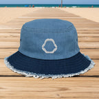 A two-tone blue bucket hat made of washed light blue denim on the crown and a darker navy blue denim brim with frayed edges. A white embroidered shark-tooth motif is stitched on the front center of the crown.
